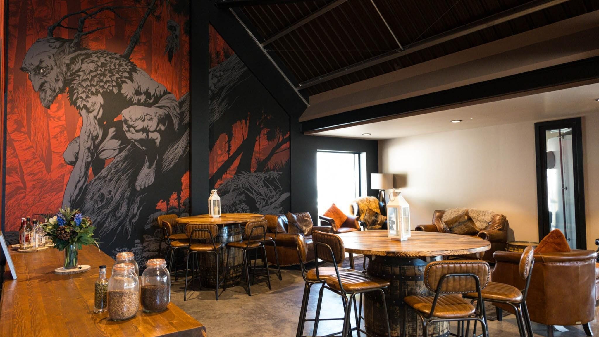 A modern dining area with a large mural, wooden tables, leather chairs, and a cozy seating area with cushions.