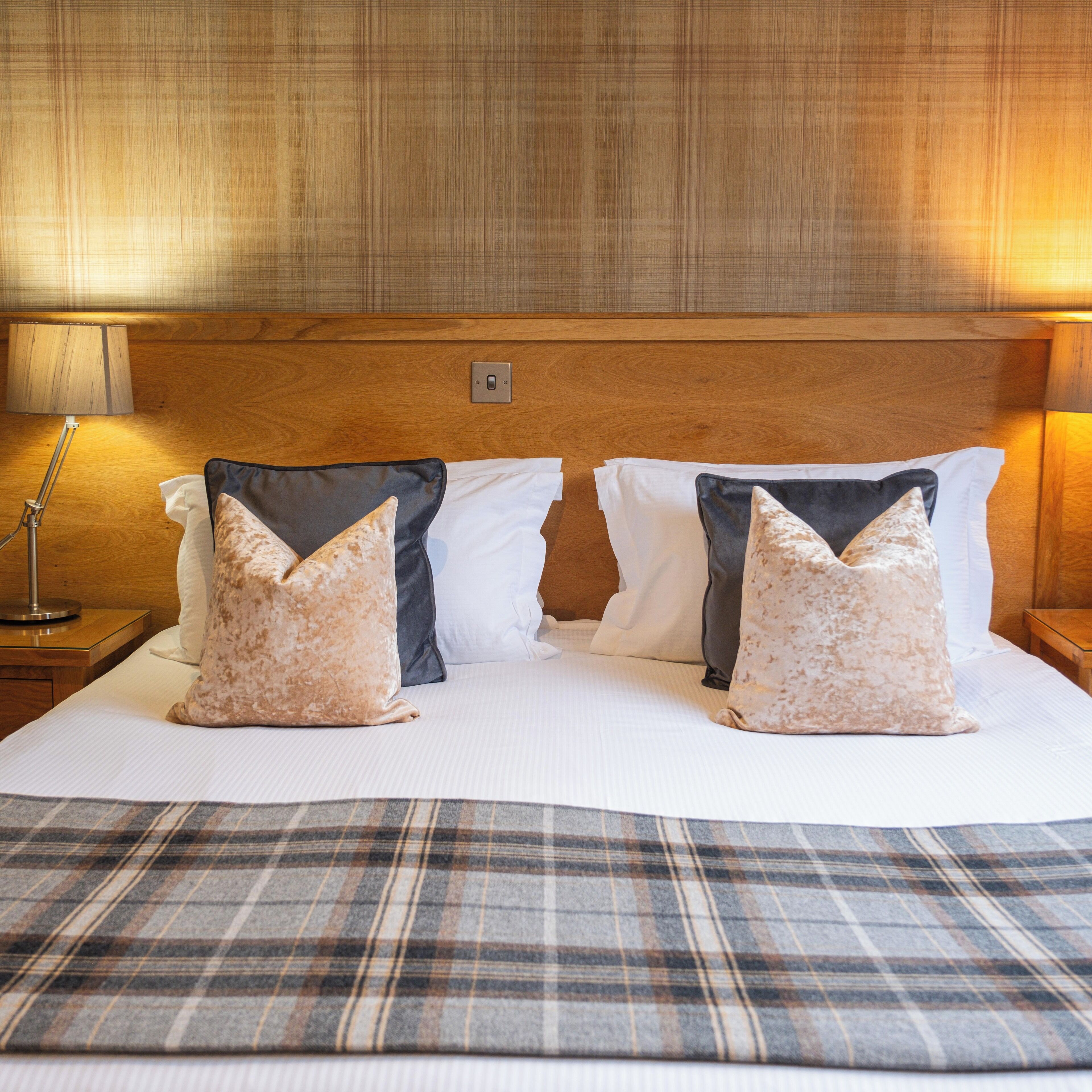 A neatly made bed with a plaid bedspread, two pillows, and a wooden headboard.