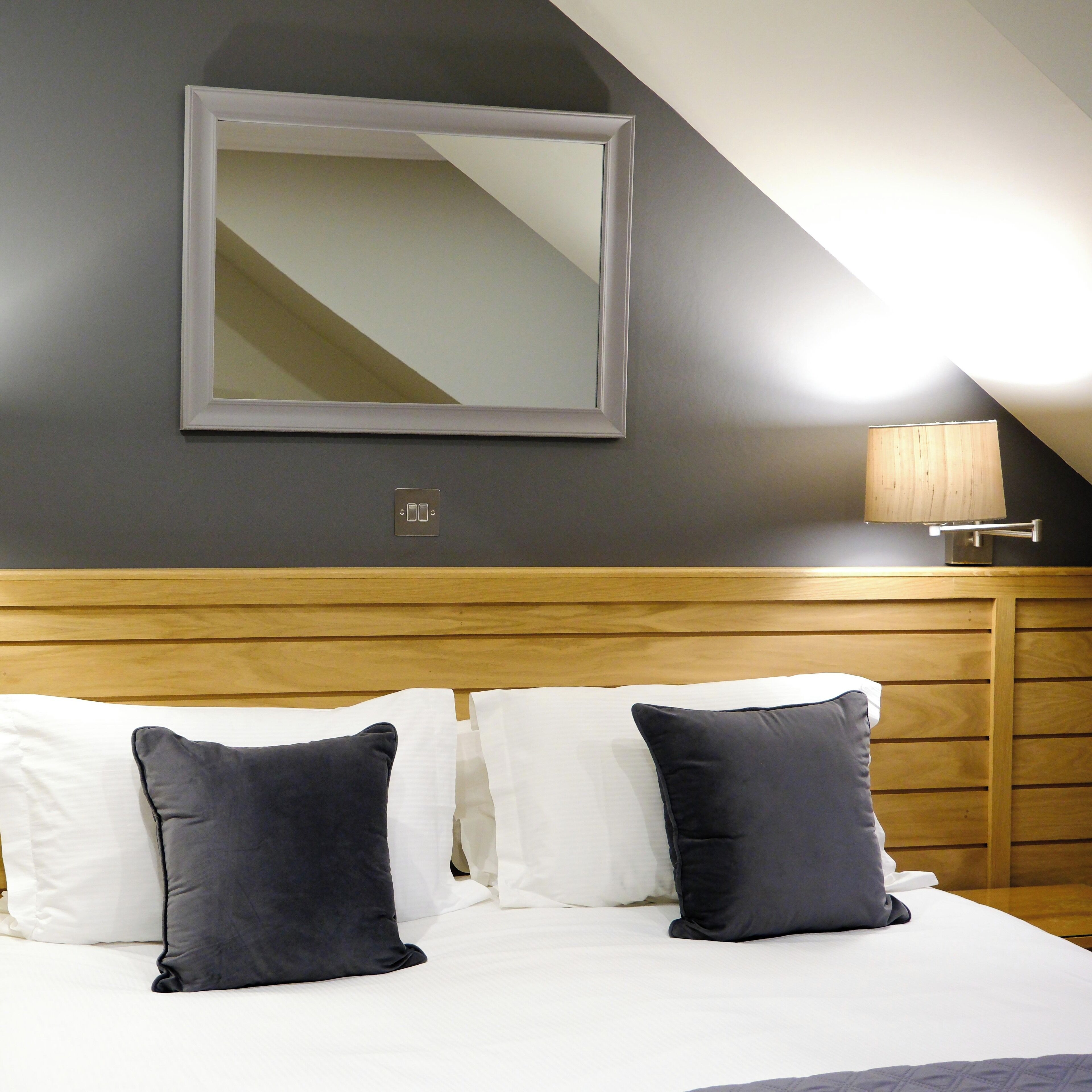 Ein Hotelzimmer mit einem Bett, Kissen, einem Holz-Kopfteil, einem Spiegel und einer Lampe.