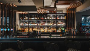 A bar with multiple shelves of liquor bottles, copper pipes, and a coffee machine.