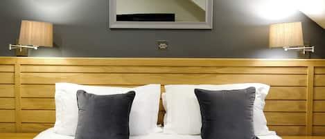 A hotel room with a bed, two bedside lamps, a mirror, and a wooden headboard.