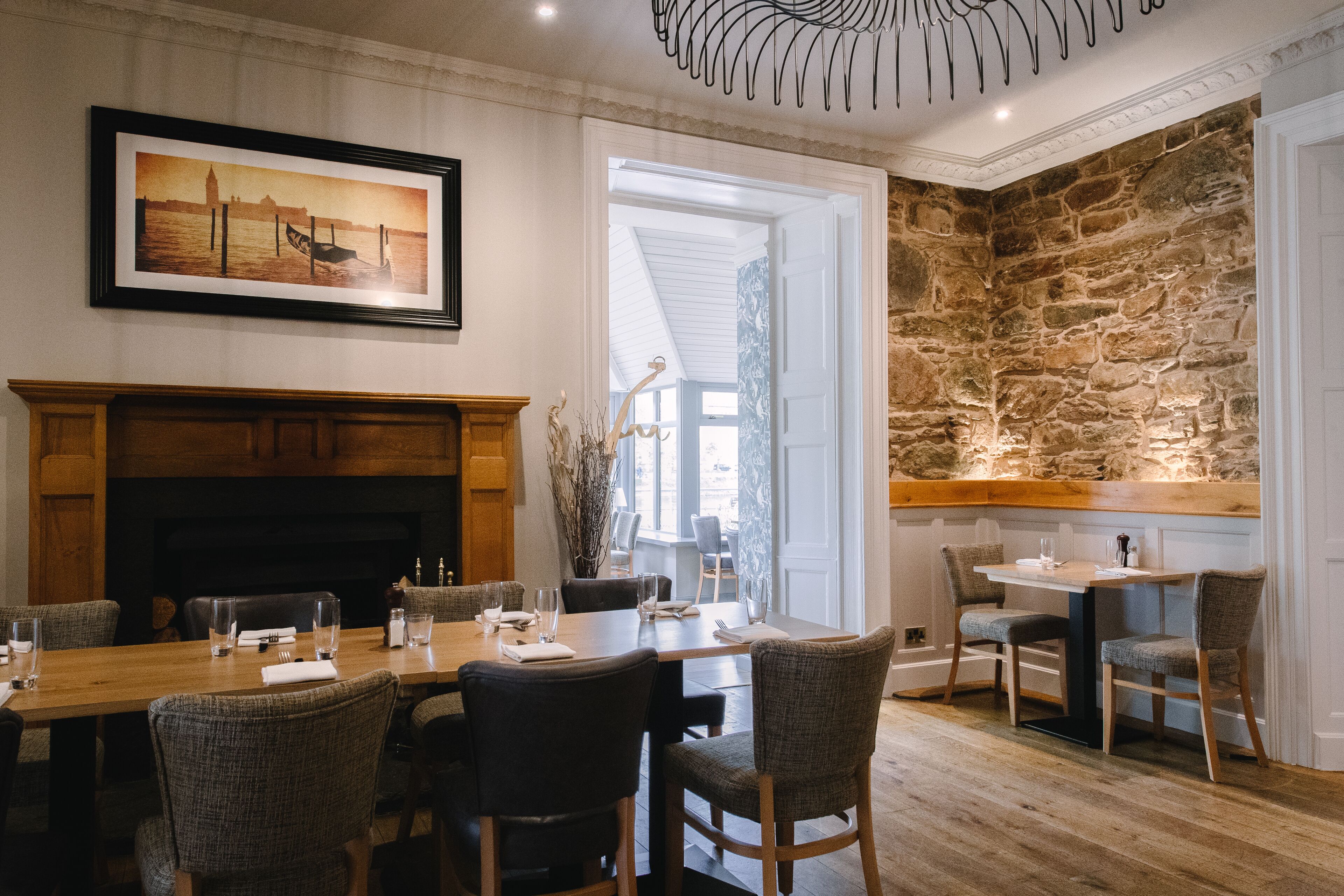 A dining area with a long wooden table, multiple chairs, a fireplace, and a stone wall.