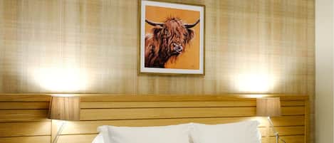 A hotel room with a bed, two bedside lamps, a wooden headboard, and a painting of a bull on the wall.