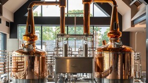 A distillery with copper stills and a large window overlooking a stone wall.