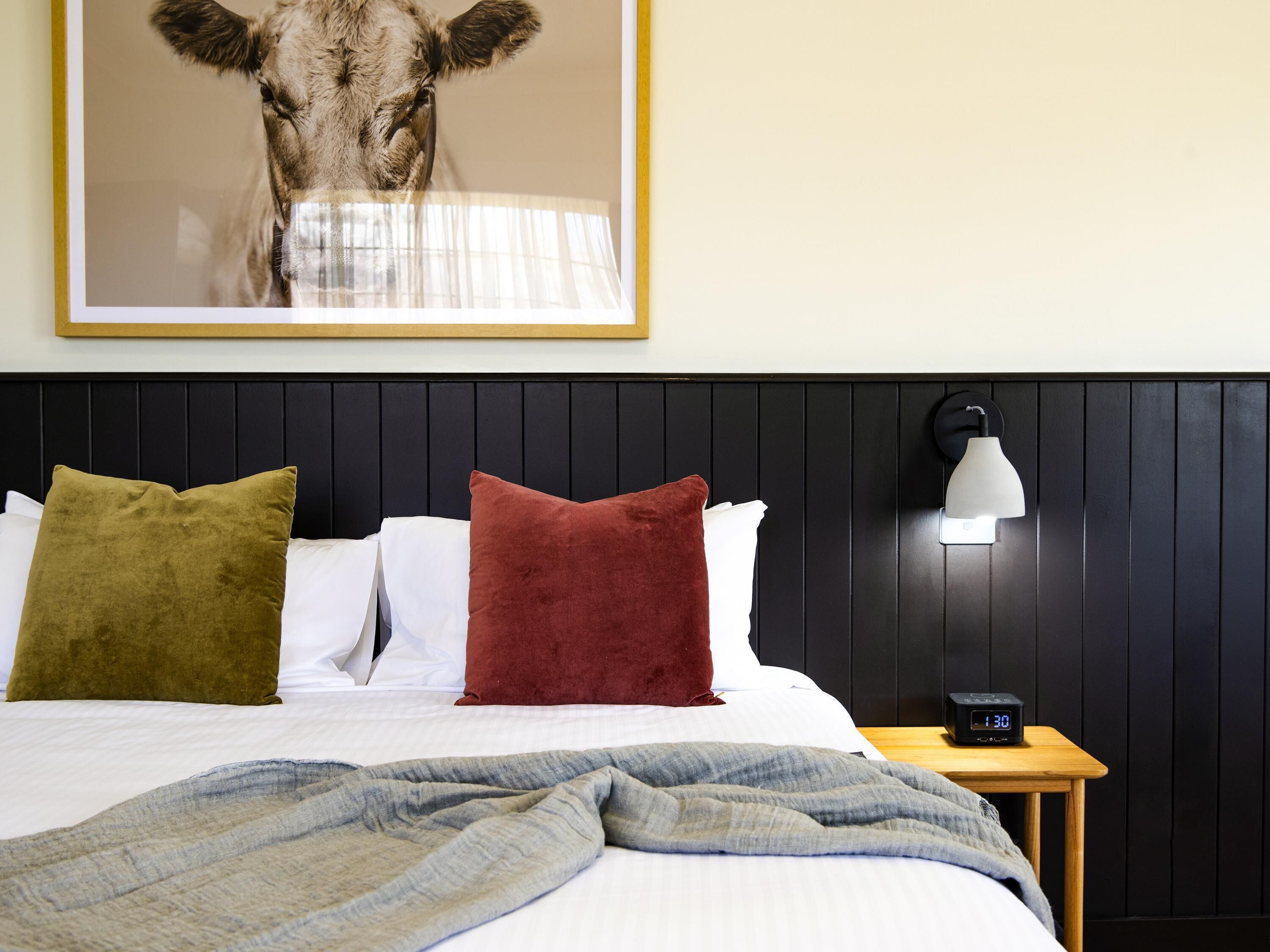 A neatly made bed with pillows, a bedside lamp, and a clock on a wooden nightstand.