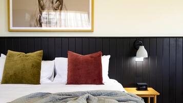A neatly made bed with pillows, a bedside lamp, and a clock on a wooden nightstand.