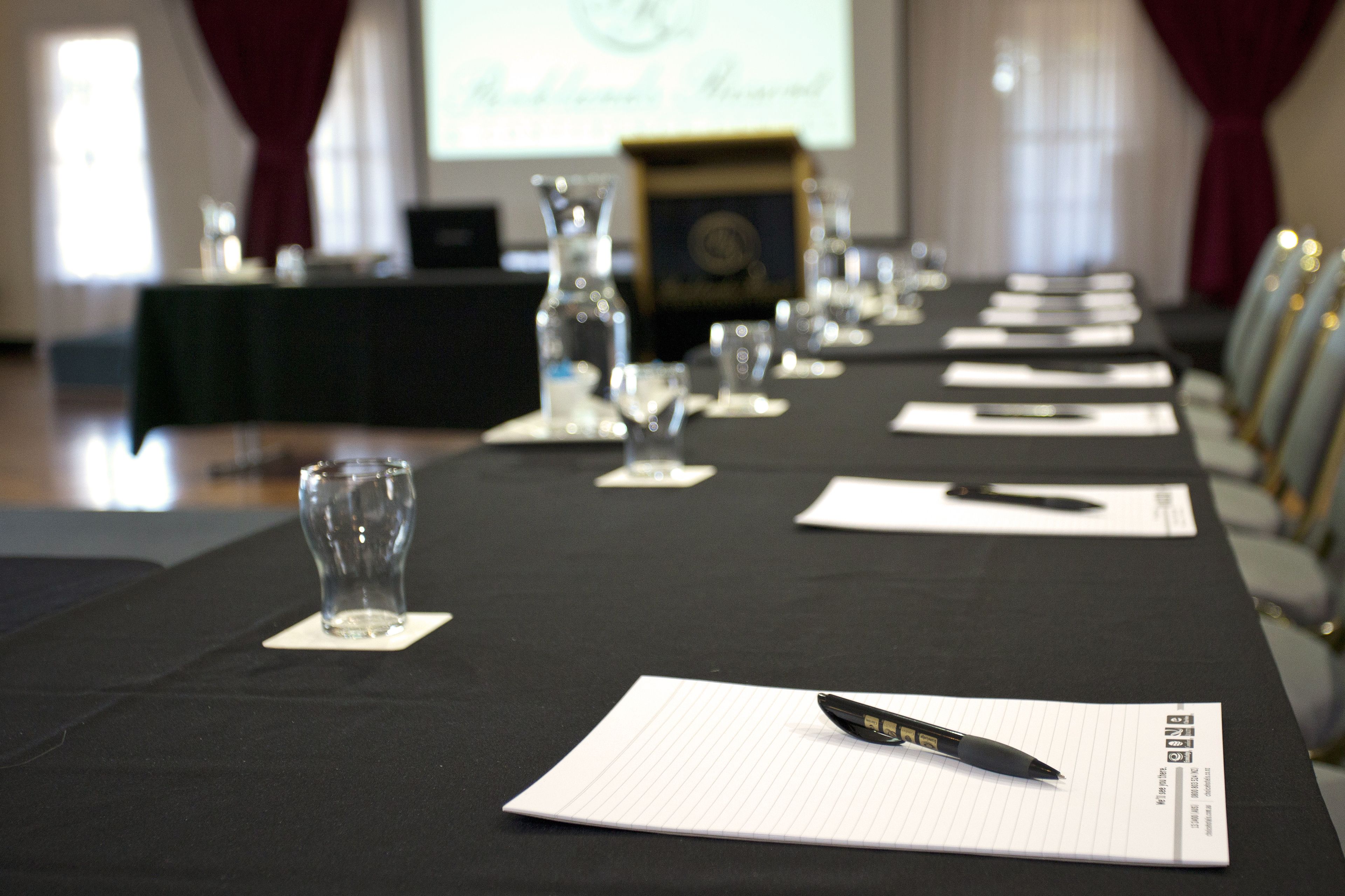 Un salón de conferencias con una larga mesa dispuesta para una reunión, con vasos y blocs de notas.