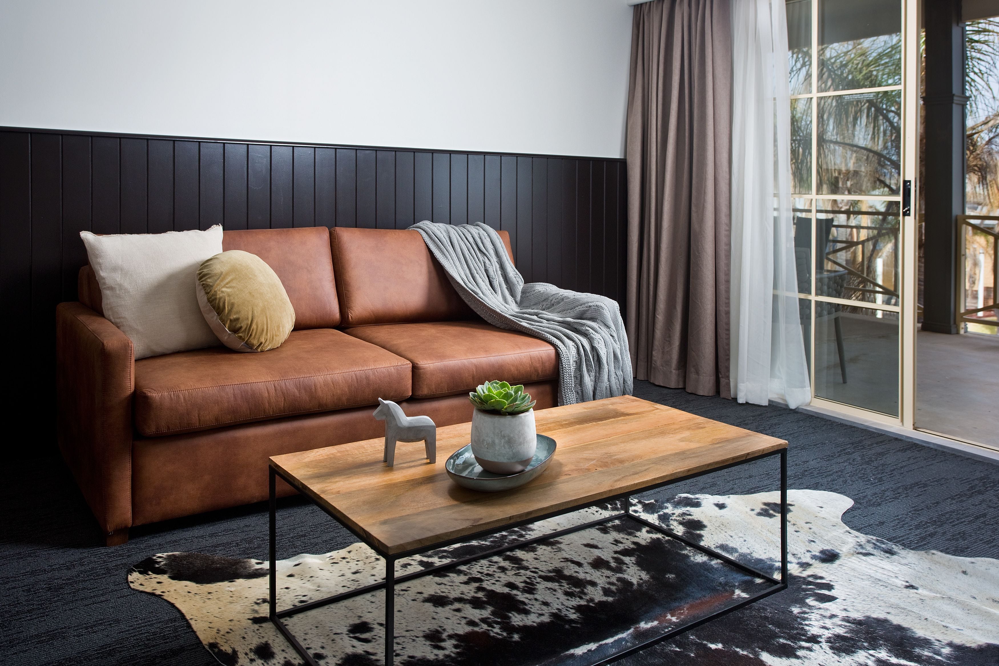 A modern living room with a brown leather sofa, a wooden coffee table, and a cowhide rug.