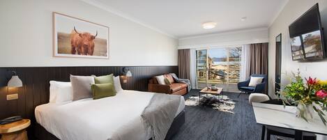 Ein Hotelzimmer mit einem großen Bett, einem Schreibtisch, einem Sessel, einem Fernseher und einem Balkon mit Blick.