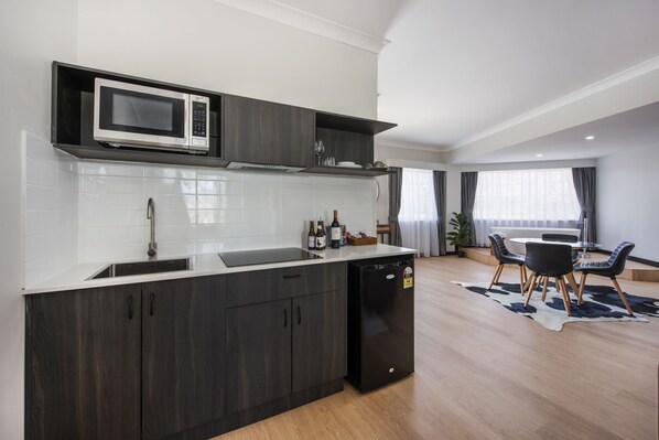 A modern kitchen with dark wood cabinets, a built-in microwave, and a dishwasher. There is a dining area with a round table and chairs.
