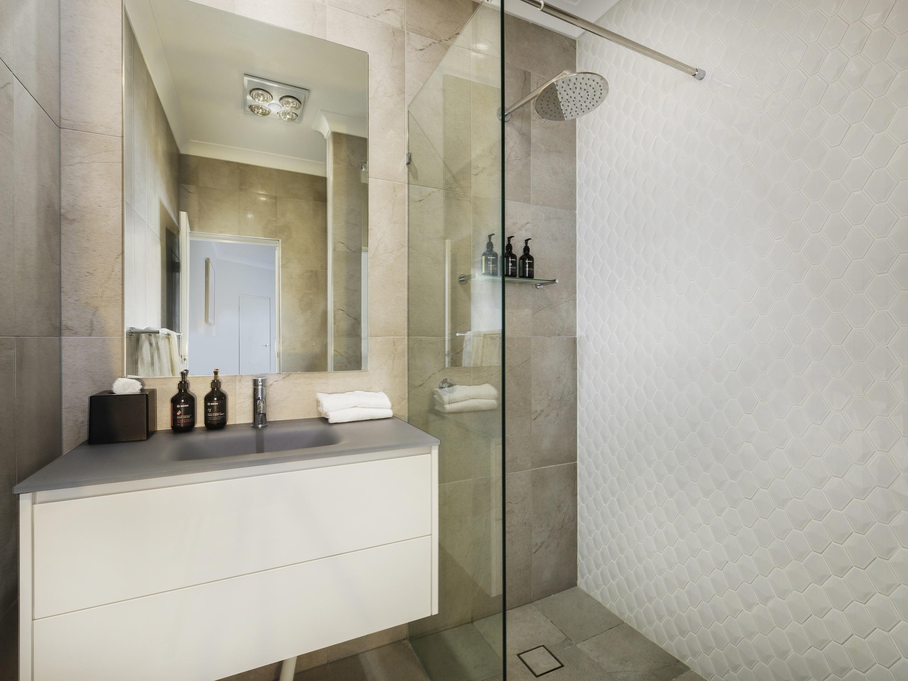 A modern bathroom with a glass shower enclosure, a vanity with a mirror, and a tiled floor.