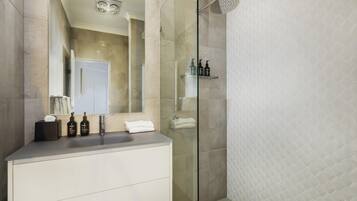 A modern bathroom with a glass shower enclosure, a vanity with a mirror, and a tiled floor.