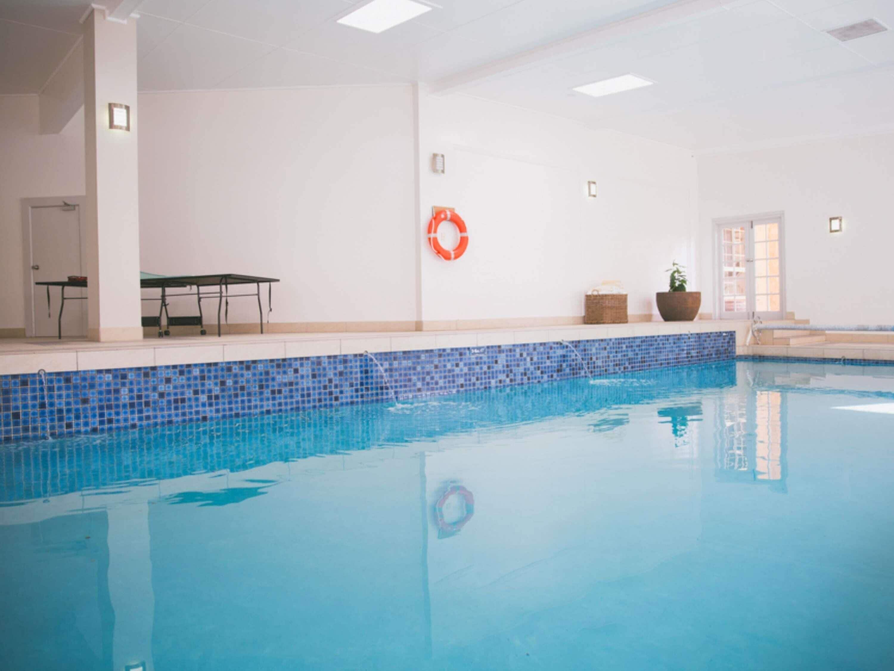 An indoor swimming pool with a tiled edge, a lifebuoy on the wall, and a bench.