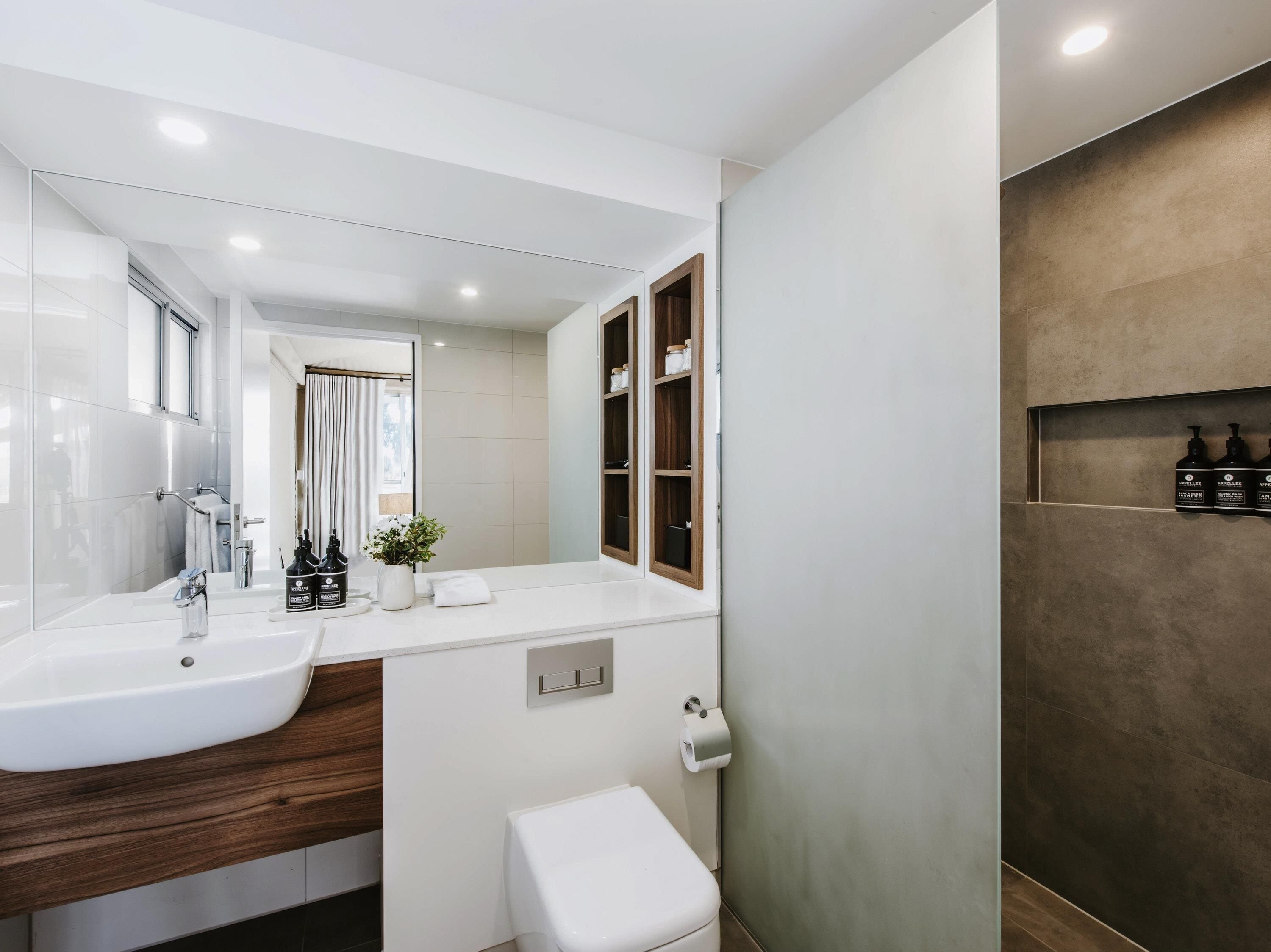 Un baño moderno con un espejo grande, dos lavamanos, un inodoro y una zona de ducha.