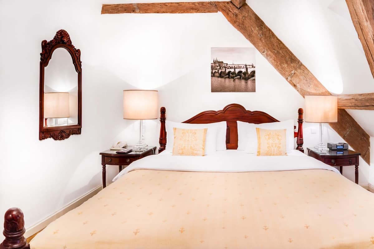 A bedroom with a large bed, wooden beams, a mirror, bedside tables, and a framed picture on the wall.