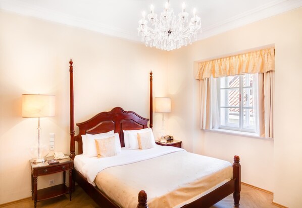 A four-poster bed with a wooden headboard, two bedside tables with lamps, a chandelier, and a window with curtains.
