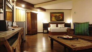 A hotel room with a wooden desk, a bed with white bedding, a painting on the wall, and a green pillow on the couch.