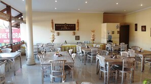 Interior de restaurante con varias mesas y sillas, un letrero que dice 'RESTAURANT de FLORA' y adornos en las paredes.