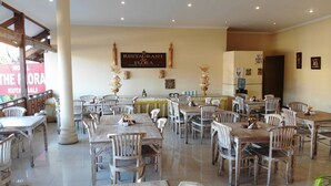 L’intérieur d’un restaurant, avec plusieurs tables et chaises, une enseigne indiquant « RESTAURANT de FLORA » et des objets décoratifs accrochés aux murs.