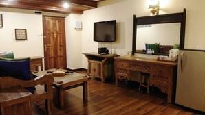 A wooden-floored room with a wooden desk, a chair, a television mounted on the wall, and a refrigerator. - The Flora Kuta Bali (Kuta)