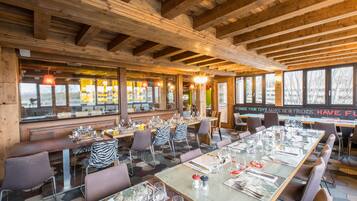 A restaurant with wooden beams, large windows, and zebra-striped chairs. Tables are set with glasses and cutlery.