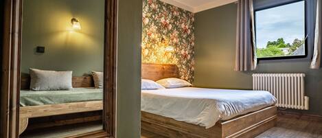 A bedroom with a wooden bed, a nightstand, a mirror, a window with curtains, and a floral wallpaper.