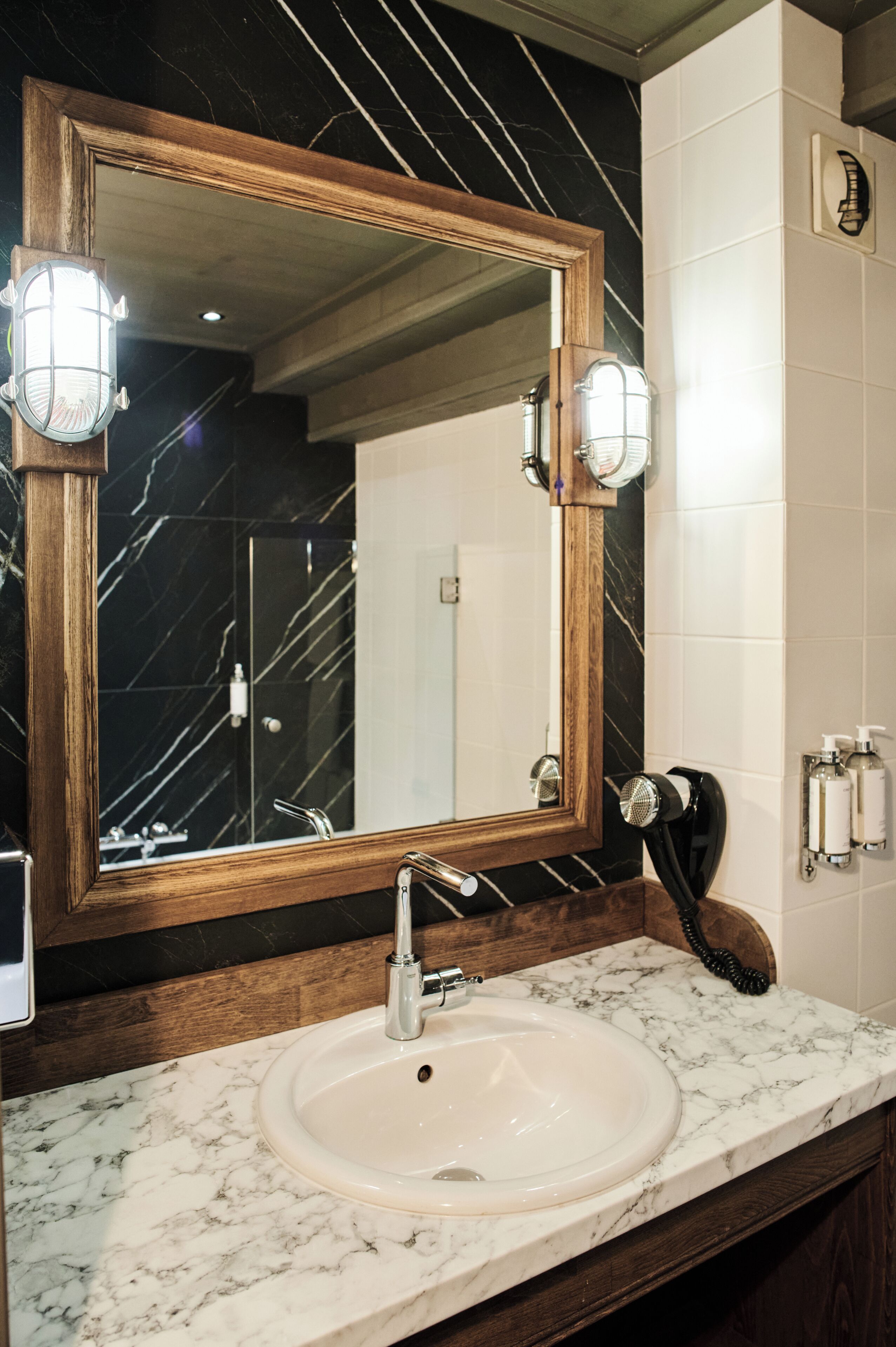 Un baño con lavamanos de mármol, espejo con marco de madera y secador de pelo en la encimera.