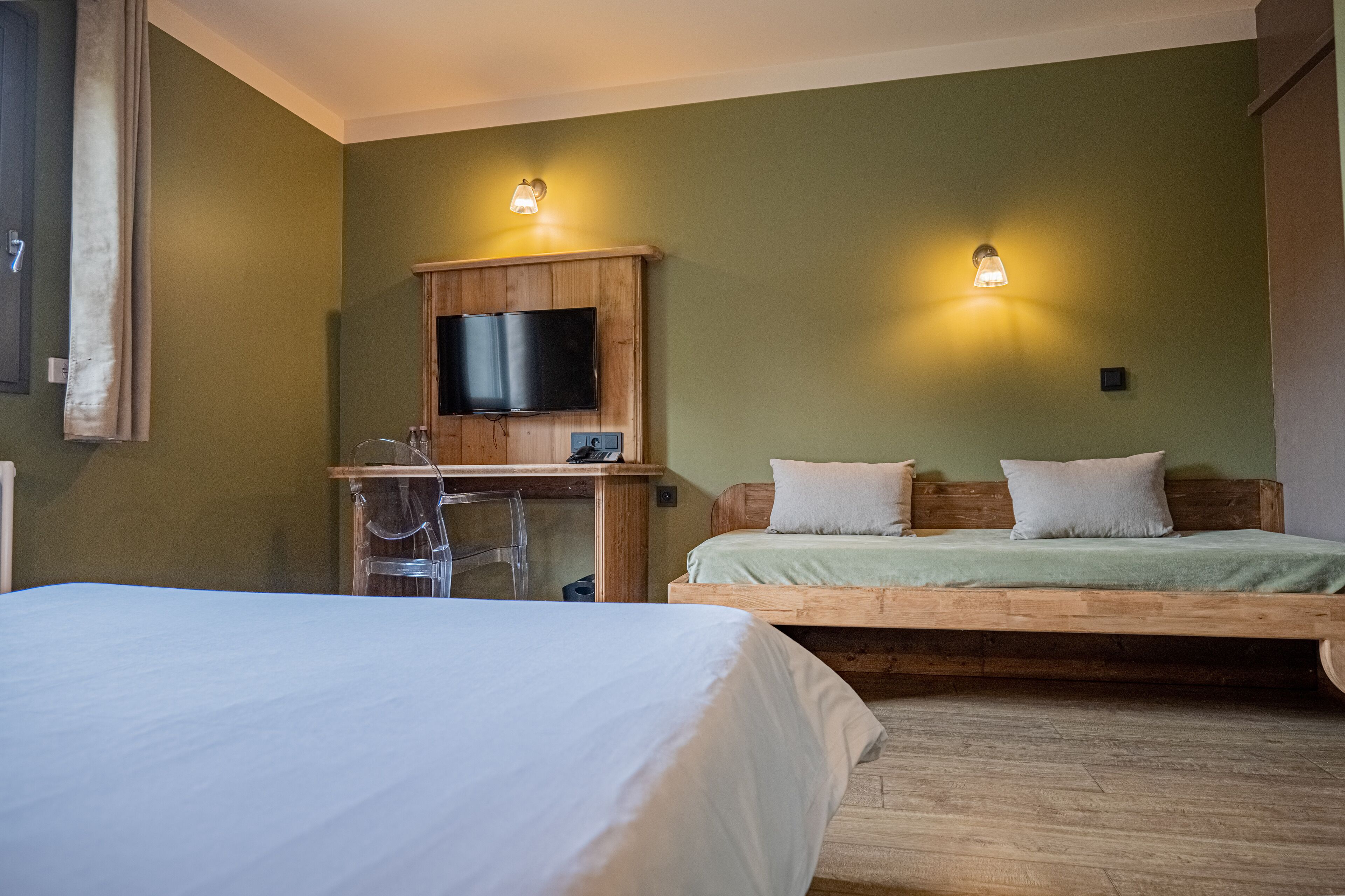A room with a bed, a desk with a chair, a television, and two wall-mounted lights.