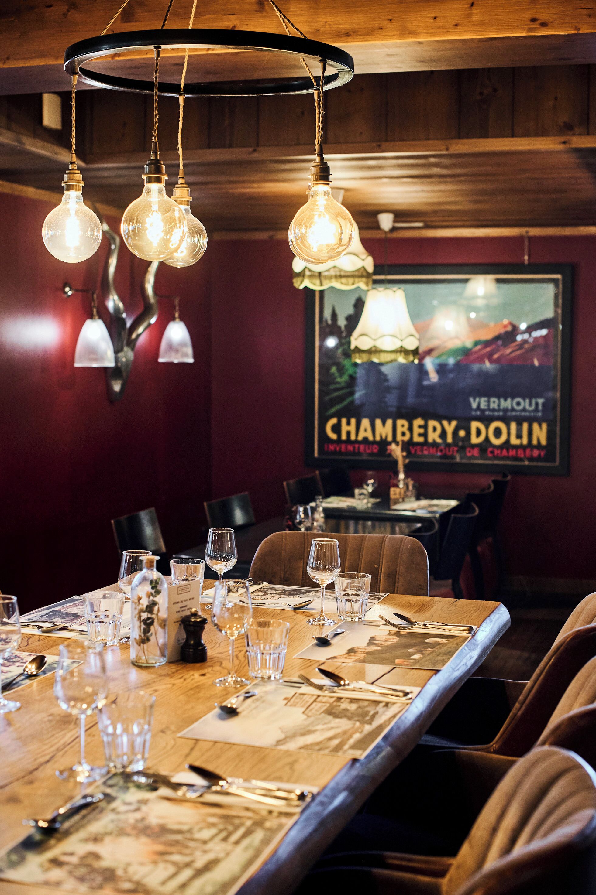 Un interior de restaurante con una mesa de madera dispuesta para comer, lámparas colgantes y un cartel en la pared.