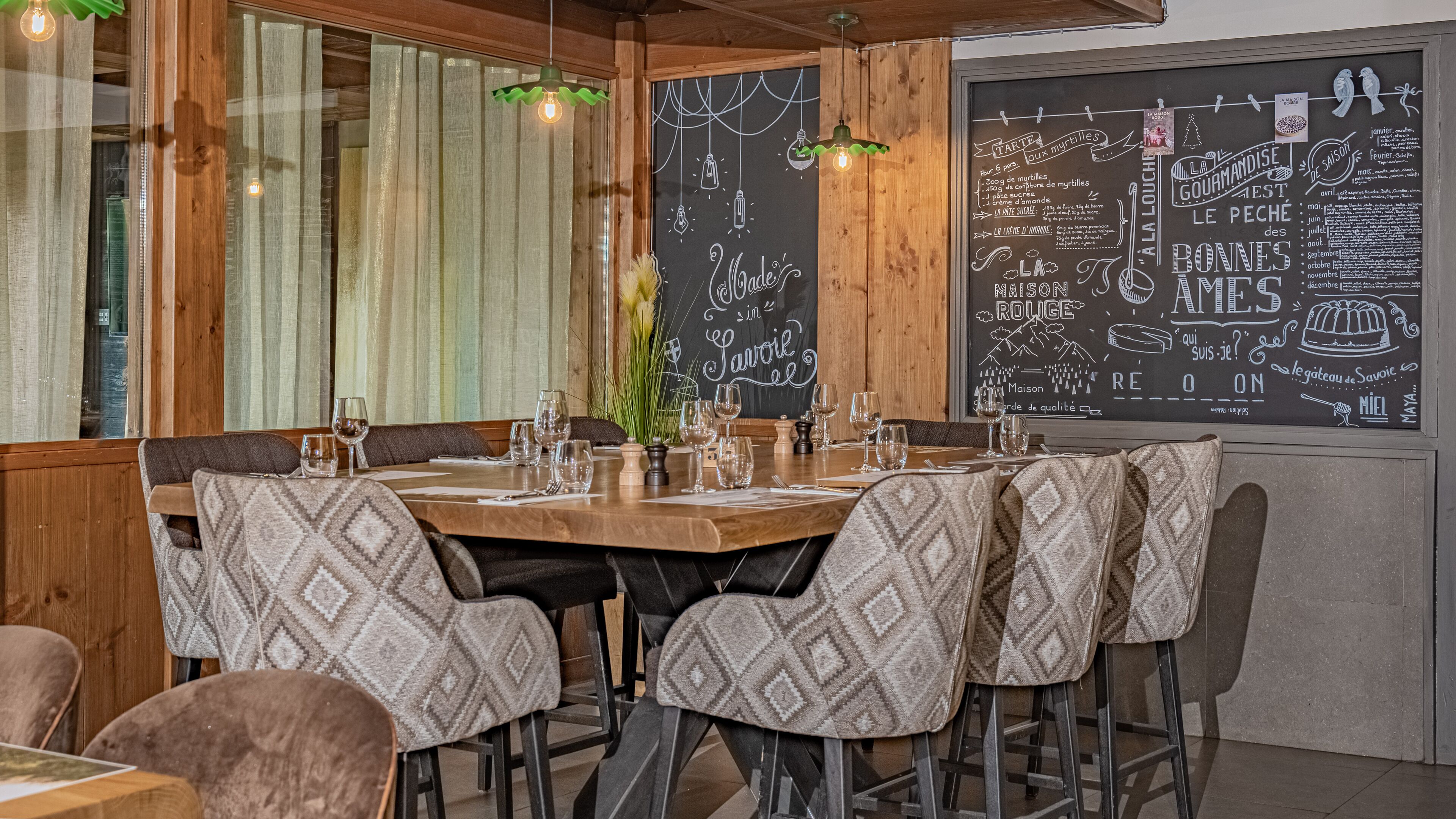 A restaurant interior with a wooden table set for dining, surrounded by patterned chairs.