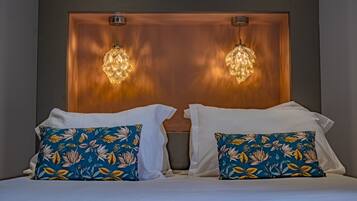 A double bed with white linens and floral-patterned pillows, a wooden headboard, and two hanging crystal chandeliers.