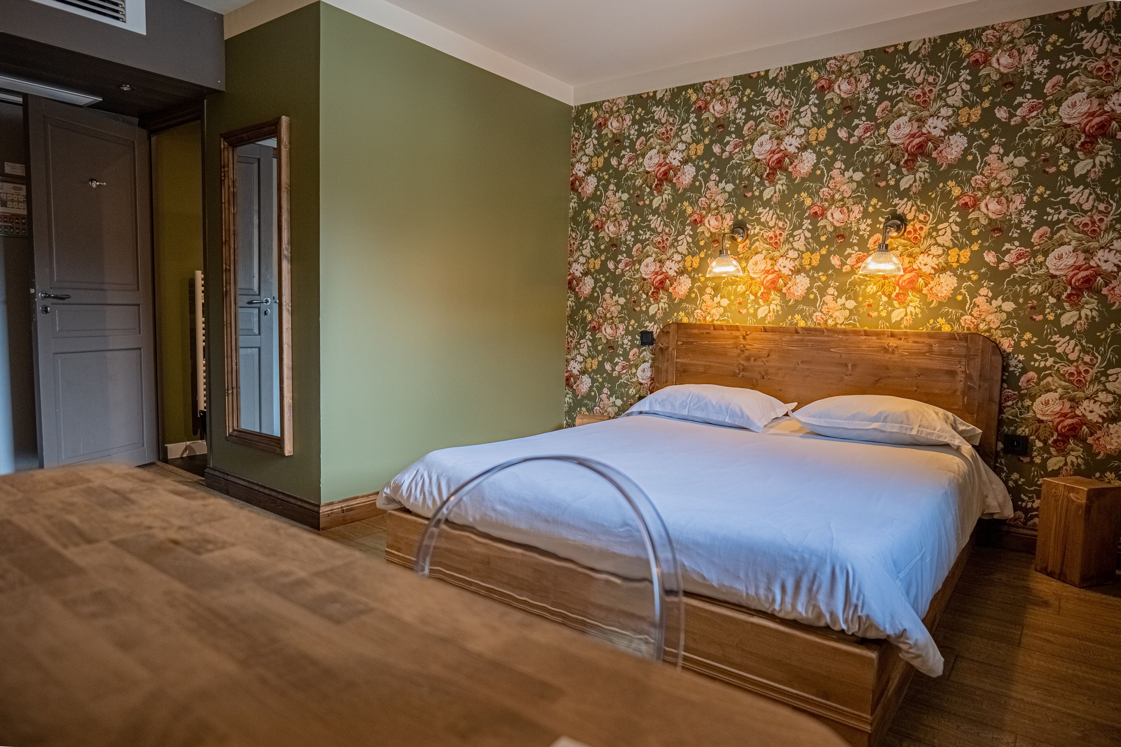 A bedroom with a wooden bed, green walls, floral wallpaper, and a wooden nightstand.
