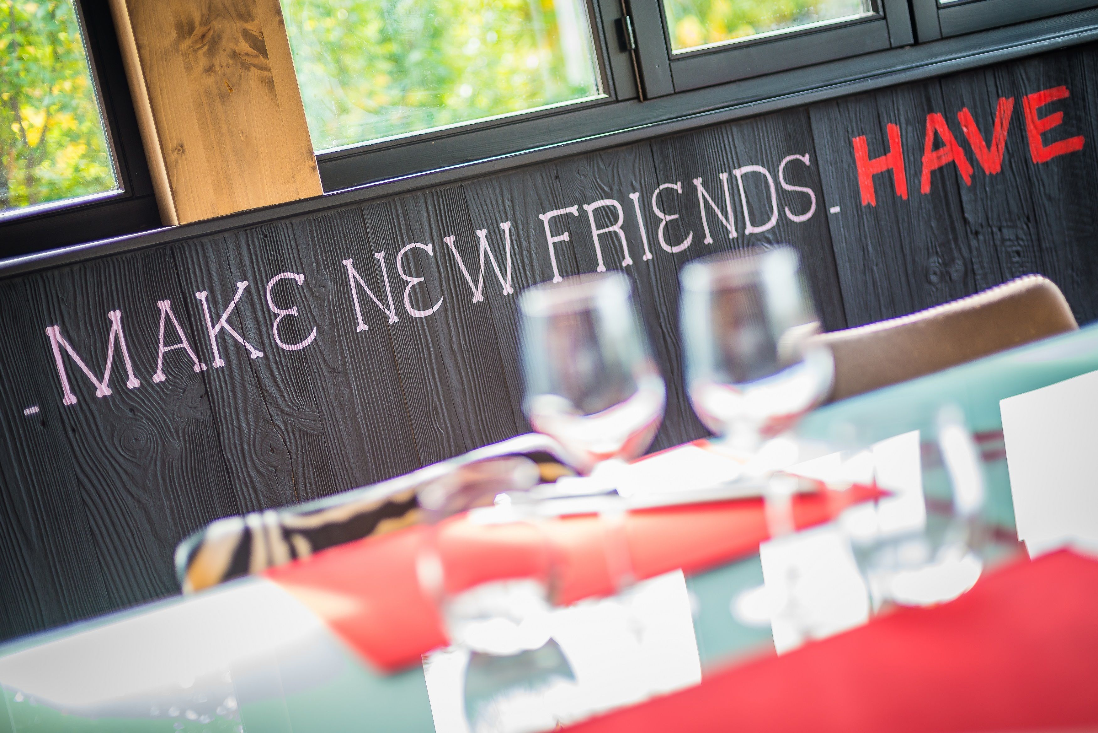 A restaurant interior with a wooden wall and a sign that reads "MAKE NEW FRIENDS. HAVE."