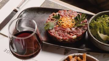 A dining table with a steak tartare dish, a glass of red wine, and a bowl of fries.