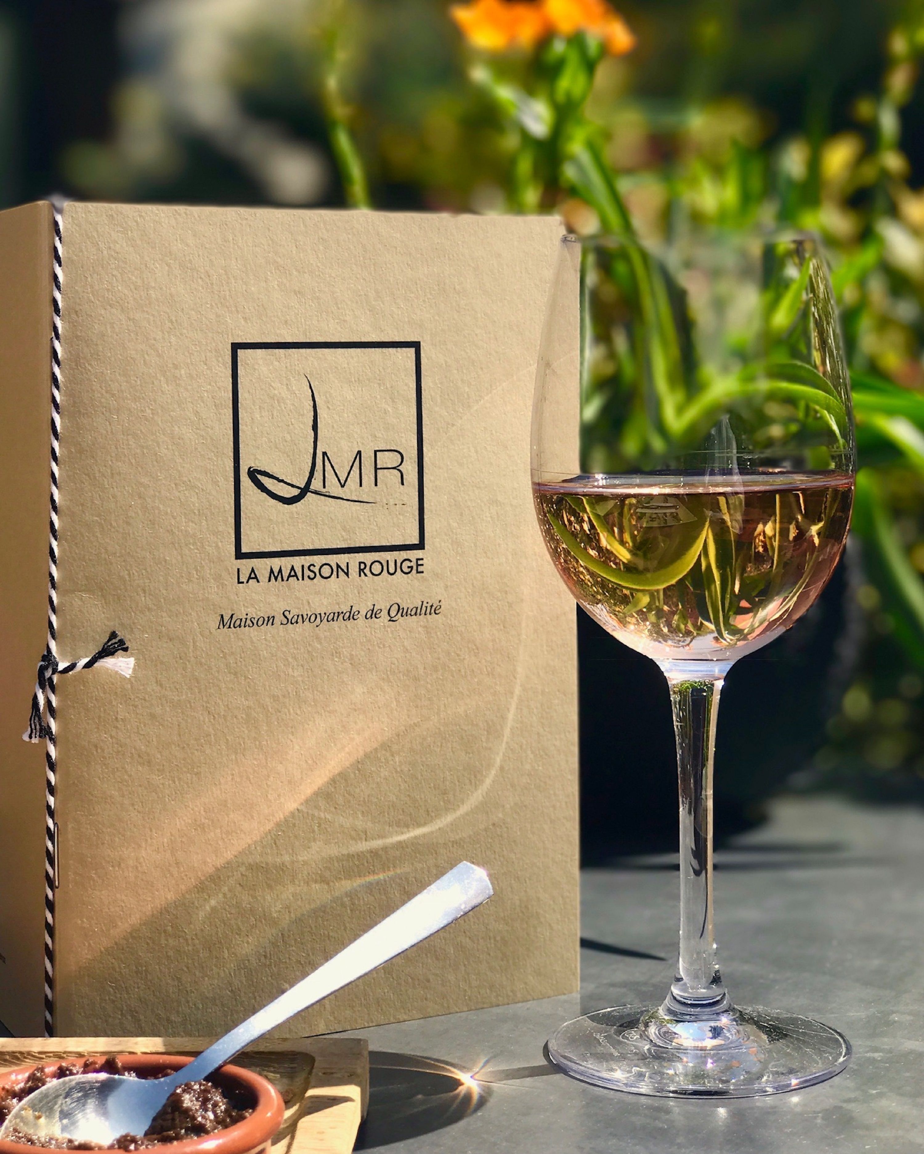 A wine glass with a spoon, a brown box with a logo, and a blurred outdoor background.