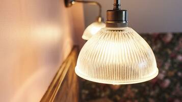 Een muurlamp met een gebogen arm en een gegroefde glazen kap, boven een houten hoofdbord en een wit kussen.