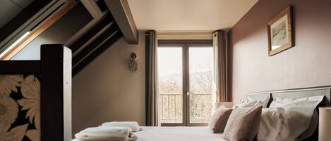 A neatly made bed with pillows and a folded towel, a bedside lamp, and a window with curtains.