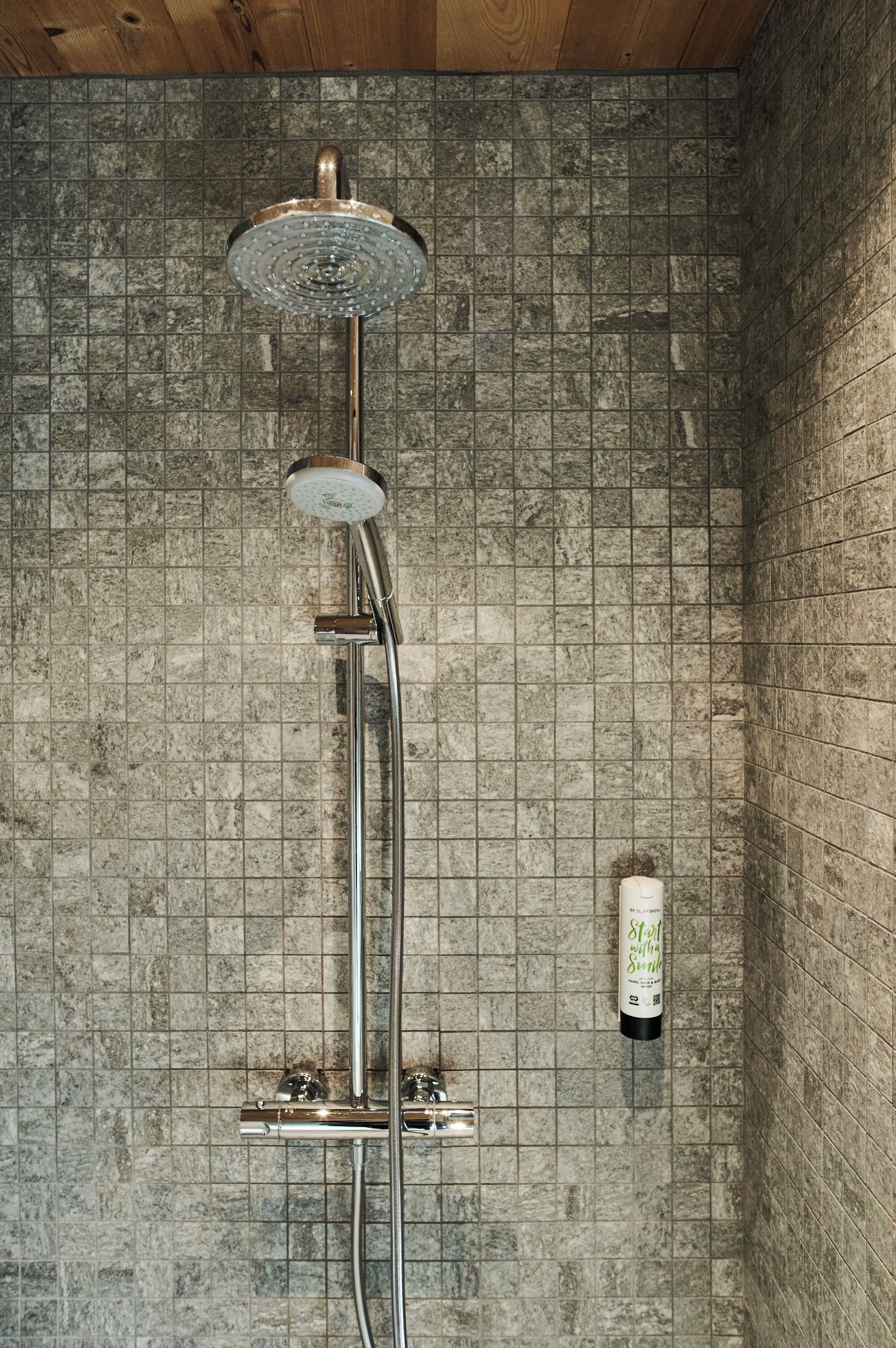 Une douche équipée d’un pommeau de douche à main et d’un panneau de commande fixé au mur.