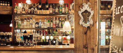 A bar area with a wooden counter, red stools, and various bottles and glasses.