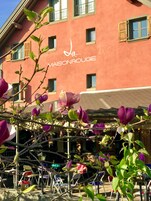 A building with a sign reading "La Maison Rouge" and a patio area with chairs and tables.