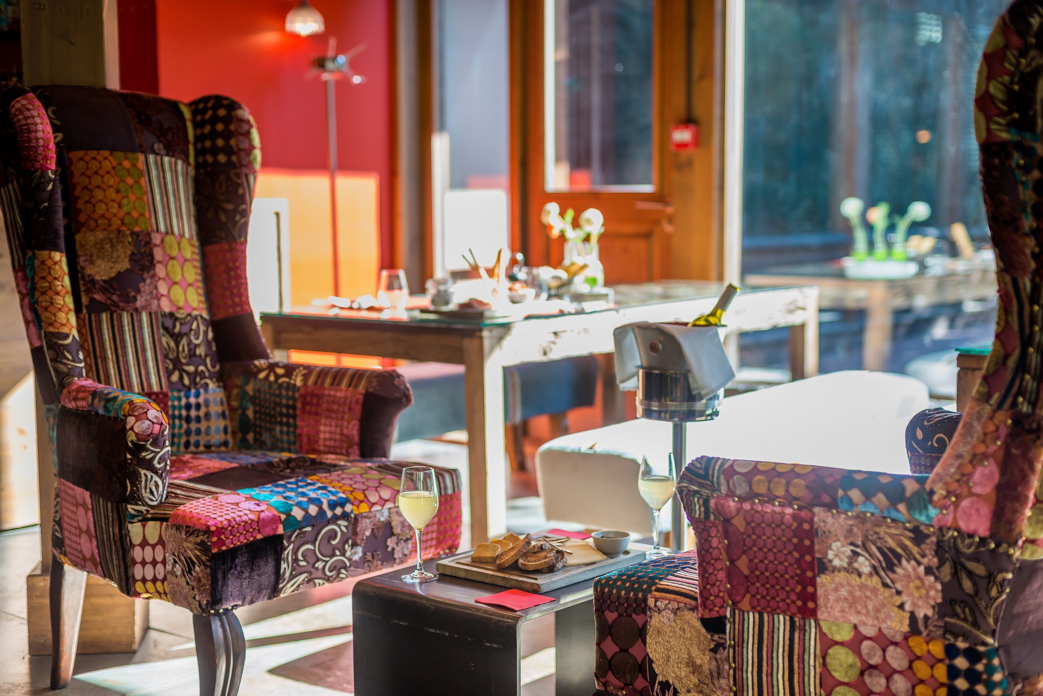 Un rincón acogedor con sillas tapizadas de colores y un patchwork, junto a una mesa con una copa de vino y aperitivos.