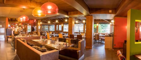 A restaurant with wooden interiors, multiple dining tables, and hanging pendant lights.