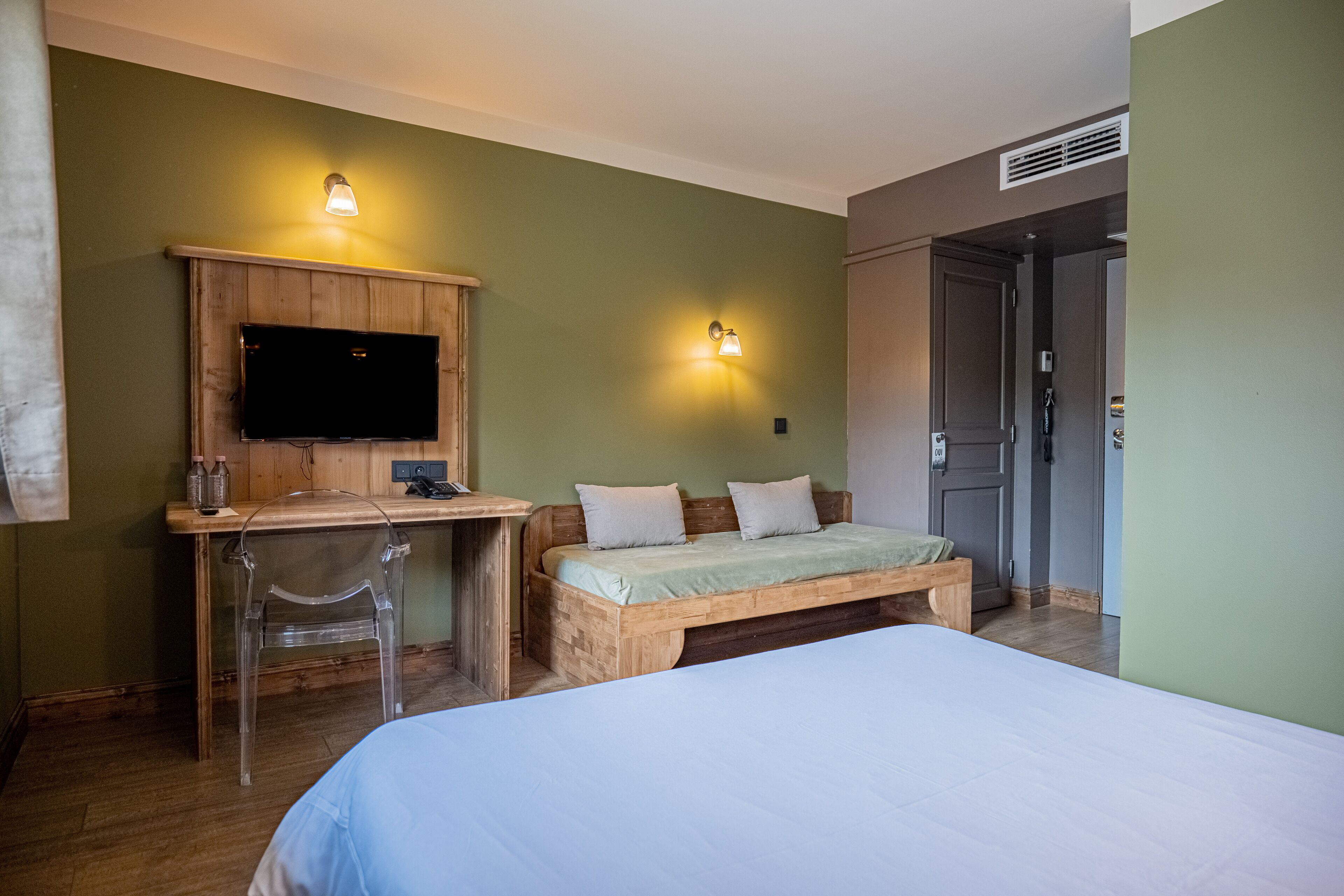 A bedroom with a bed, a wooden desk, a television, and two wall-mounted lights.