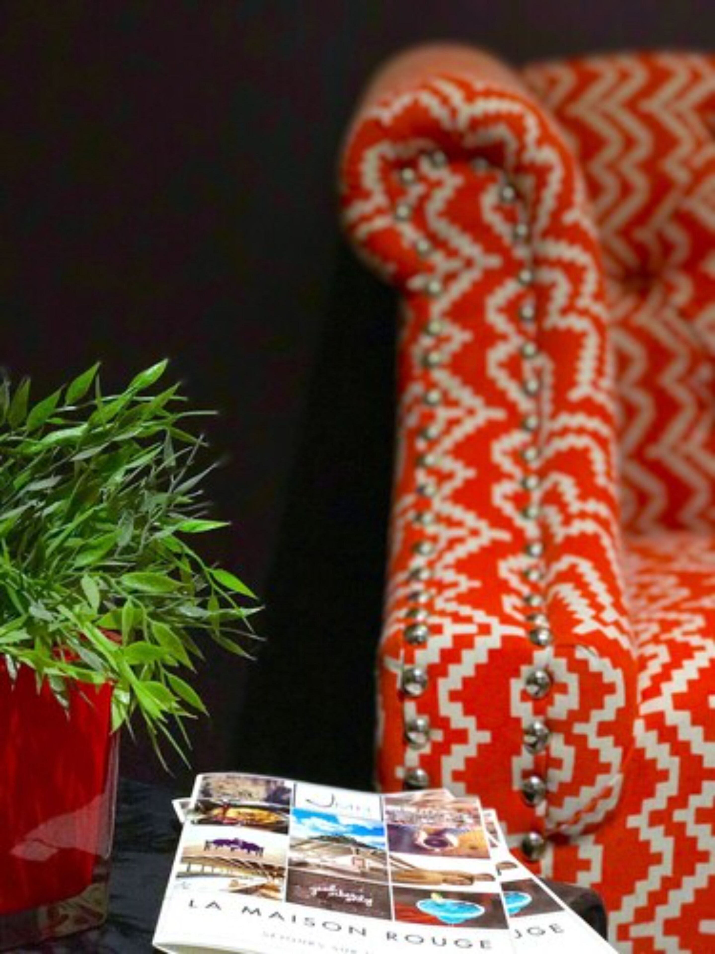 Eine Zeitschrift mit Reisefotos auf einem Tisch neben einem roten Sofa mit Muster.