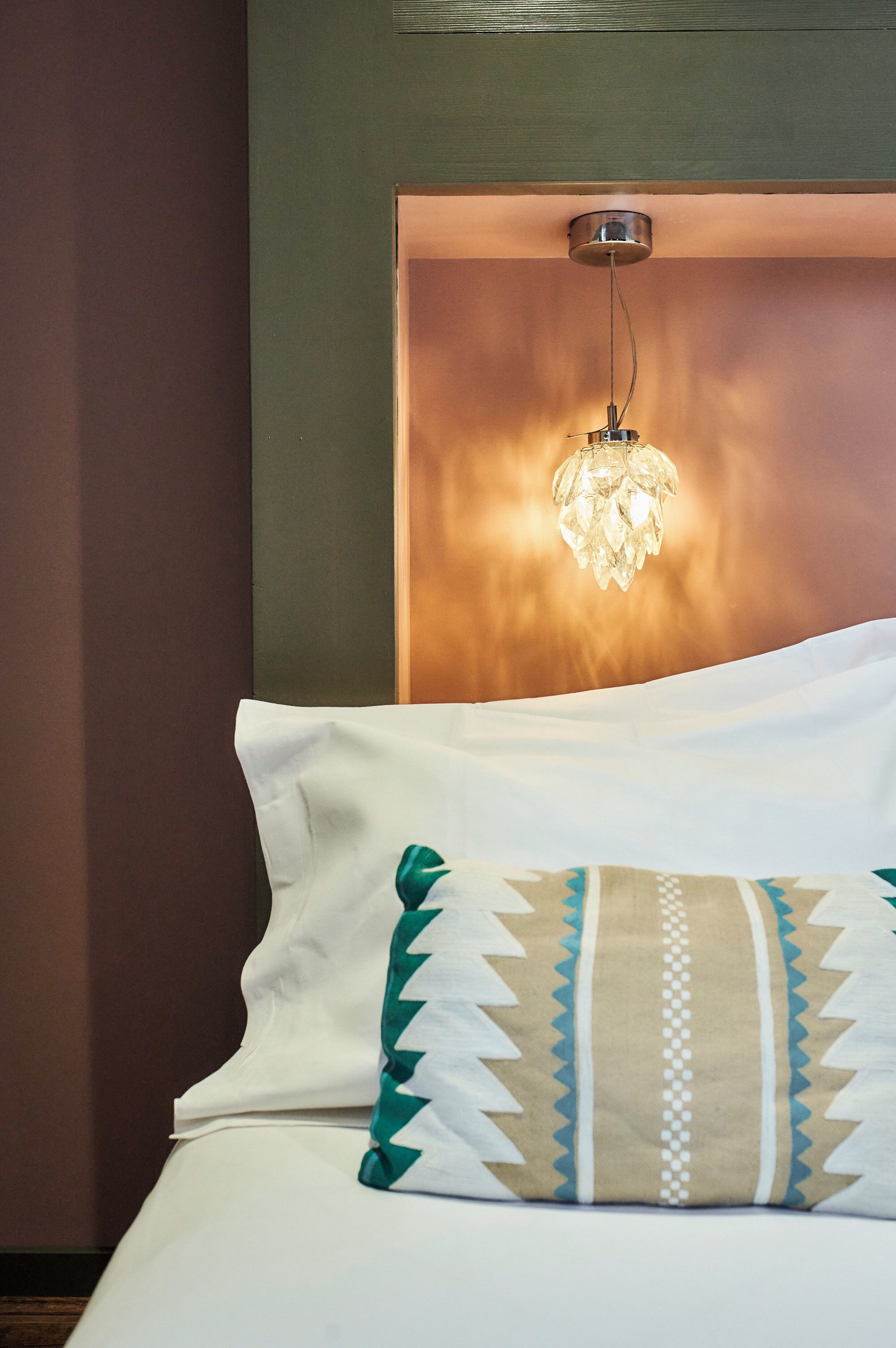 A neatly made bed with a white pillow and a patterned pillow, a headboard with a light fixture, and a wall with a textured finish.