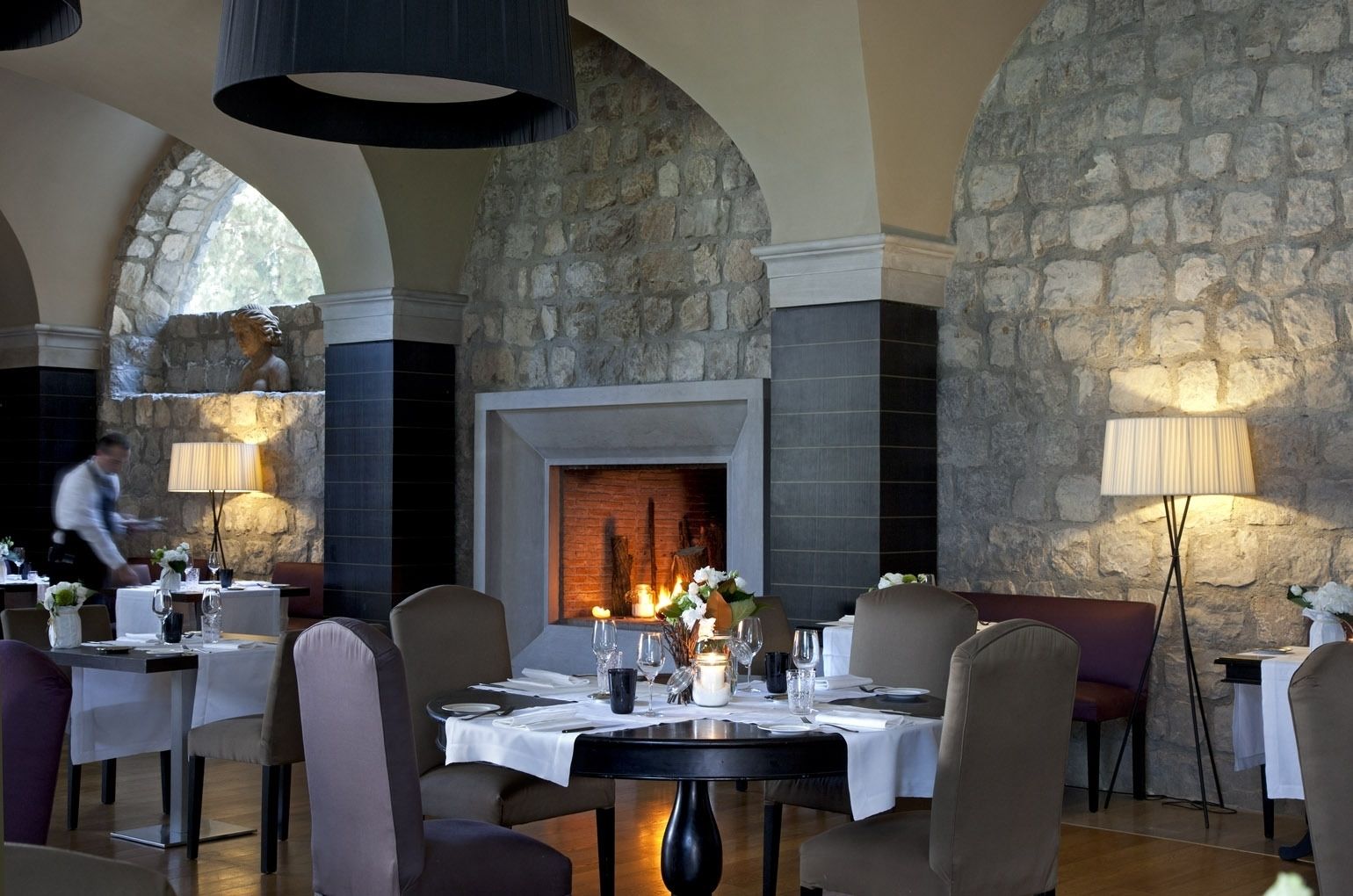 A restaurant with stone walls, a fireplace, and tables set for dining.