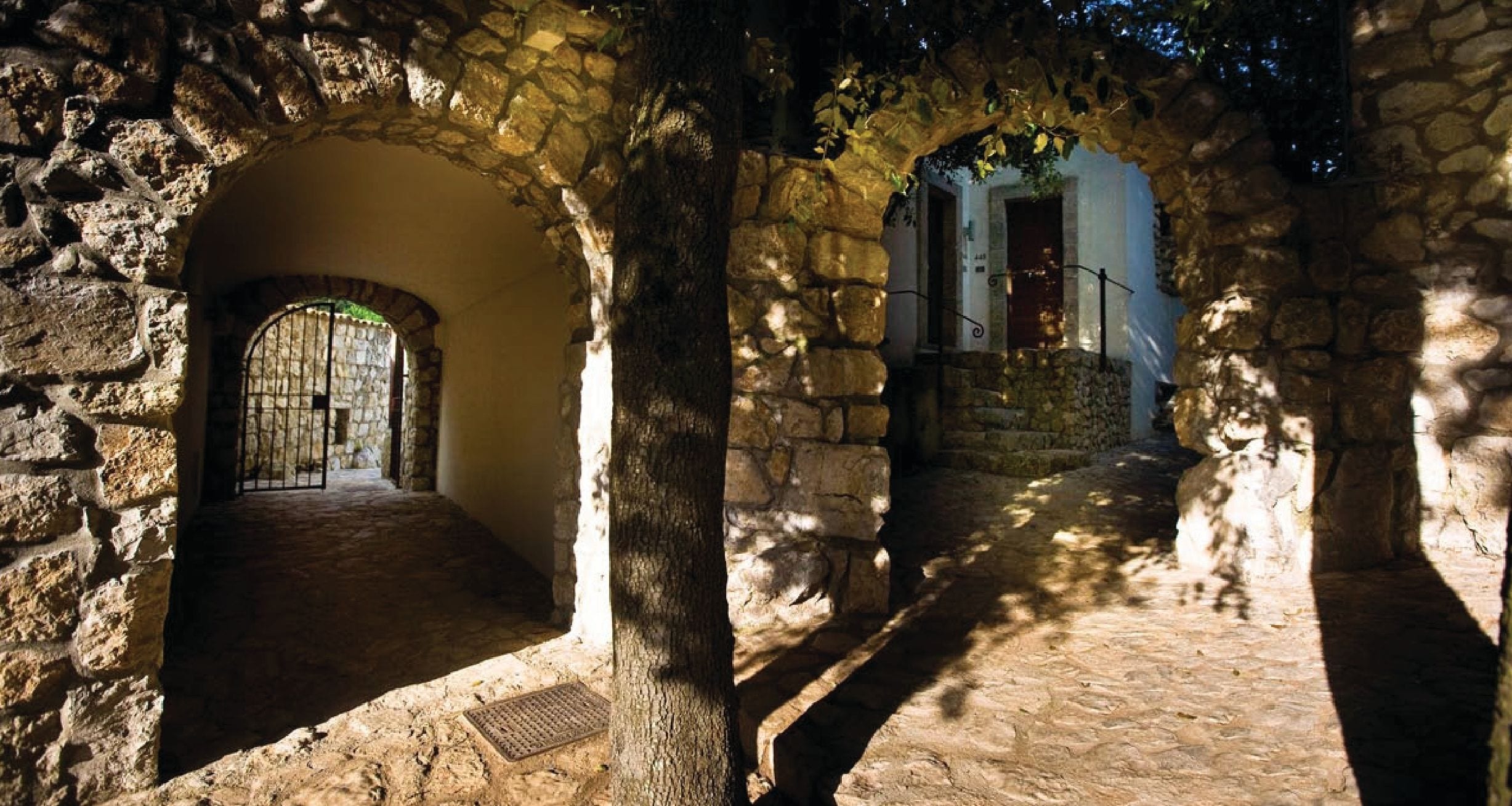 A stone corridor with arches, a metal door, and a staircase leading to a higher level.