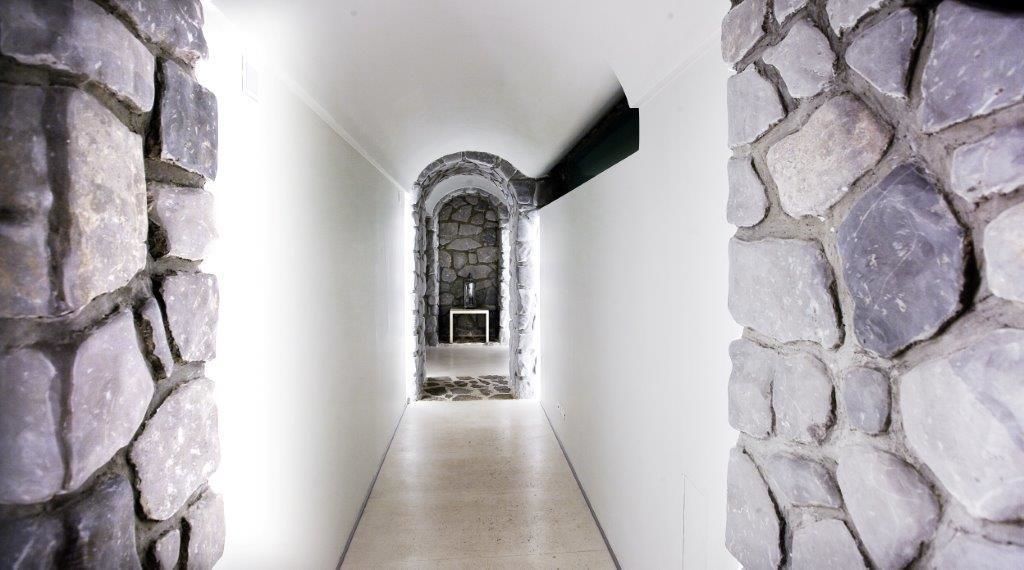 A stone-walled corridor leading to a room with a stone fireplace.