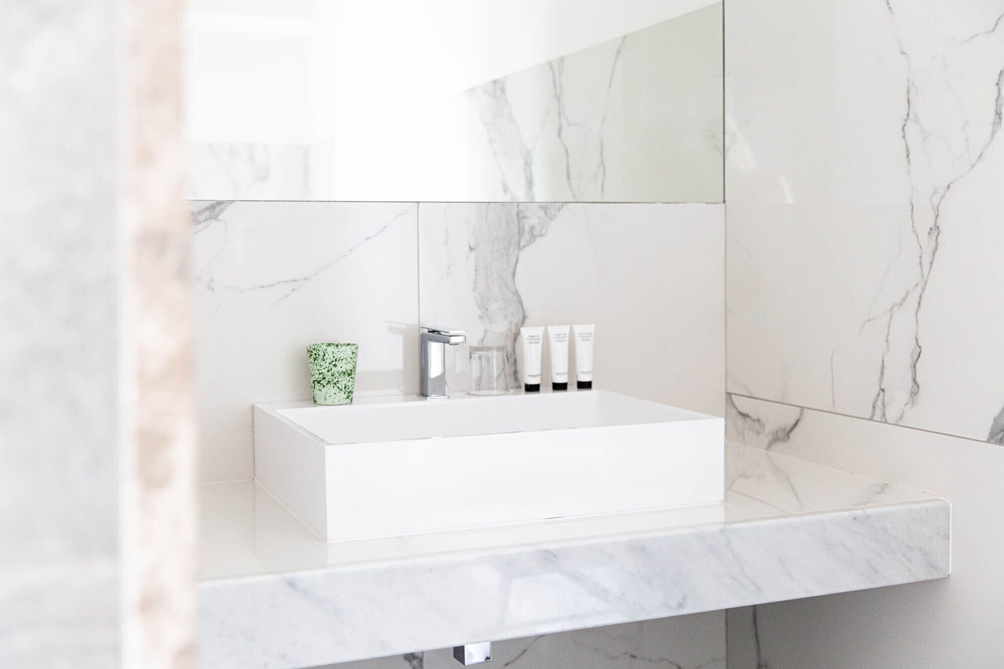 Un bagno con un lavandino in marmo bianco, un vaso verde e tre flaconi da bagno bianchi.
