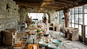 A breakfast buffet with various food items and drinks, set in a rustic stone-walled room with wicker furniture and a large window. - Aquapetra Resort and Spa (Telese)
